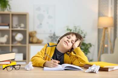 Photo of Tired little boy doing homework at table indoors