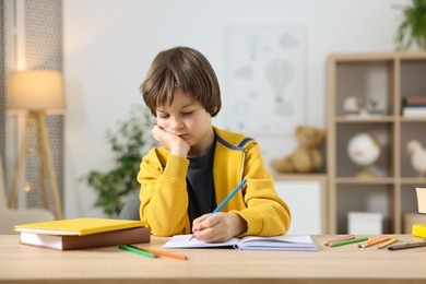 Photo of Cute little boy doing homework at table indoors