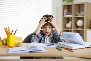Photo of Tired little boy doing homework at table indoors