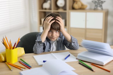 Photo of Tired little boy doing homework at table indoors