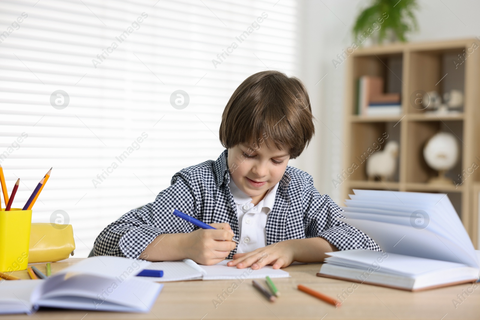 Cute little boy doing homework at table indoors Photo of Cute little boy doing homework at table indoors