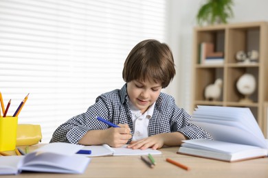 Photo of Cute little boy doing homework at table indoors