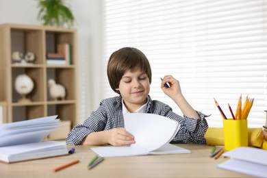 Photo of Cute little boy doing homework at table indoors