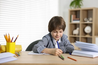 Photo of Cute little boy doing homework at table indoors