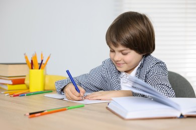 Photo of Cute little boy doing homework at table indoors