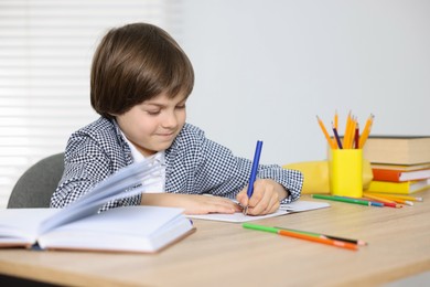 Photo of Cute little boy doing homework at table indoors