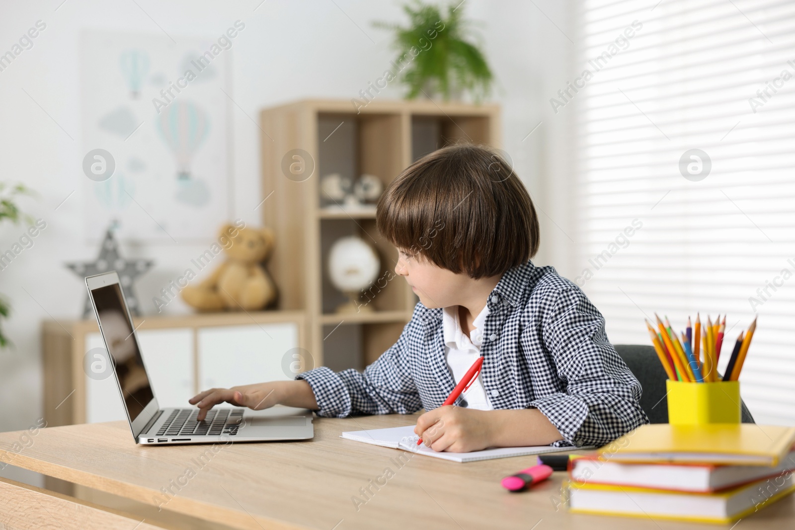 Cute little boy doing homework with laptop at table indoors Photo of Cute little boy doing homework with laptop at table indoors