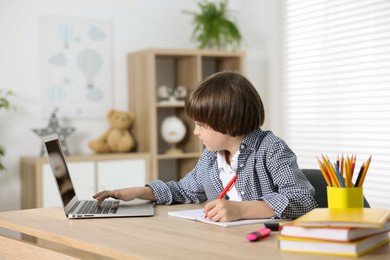 Photo of Cute little boy doing homework with laptop at table indoors