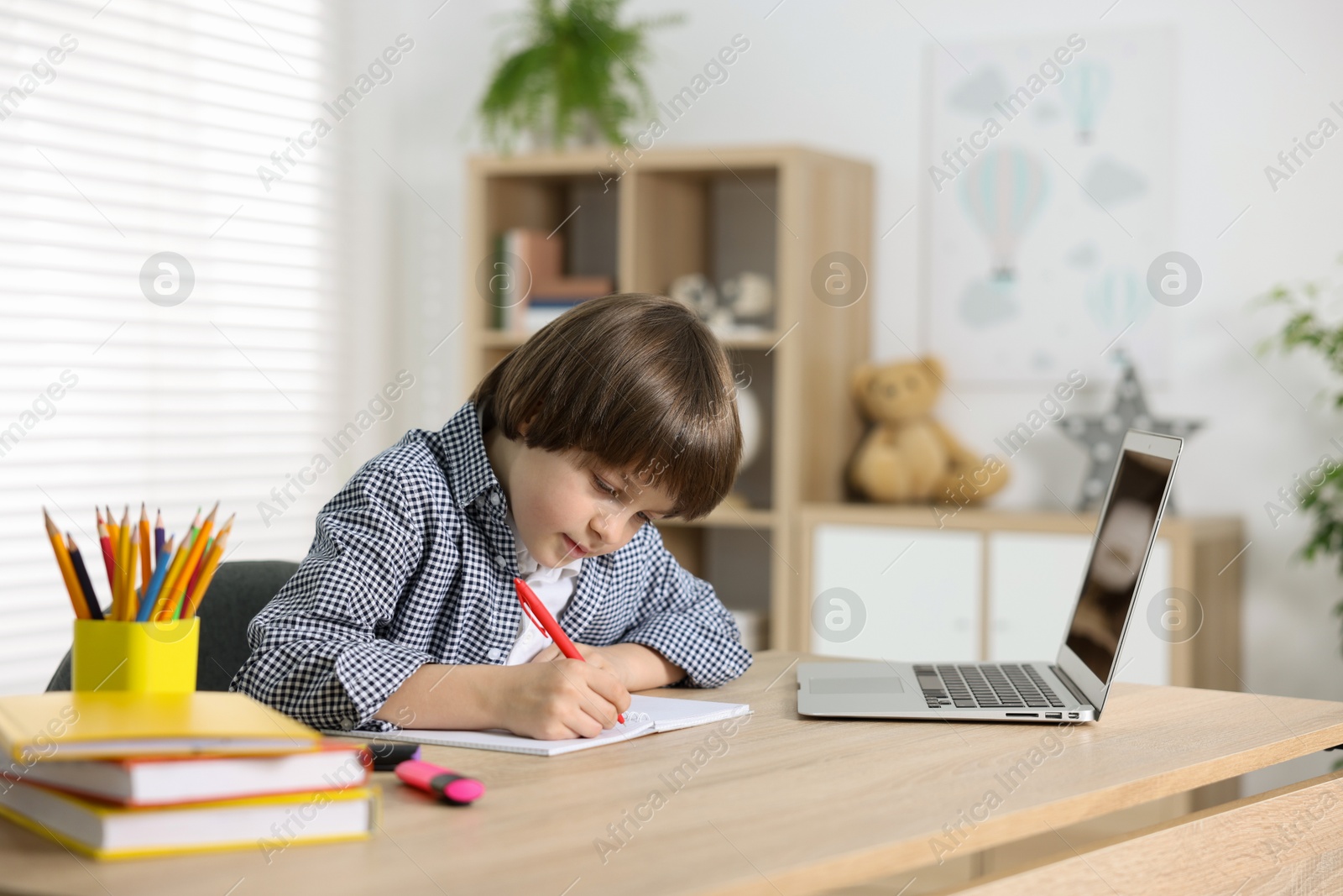 Cute little boy doing homework with laptop at table indoors Photo of Cute little boy doing homework with laptop at table indoors