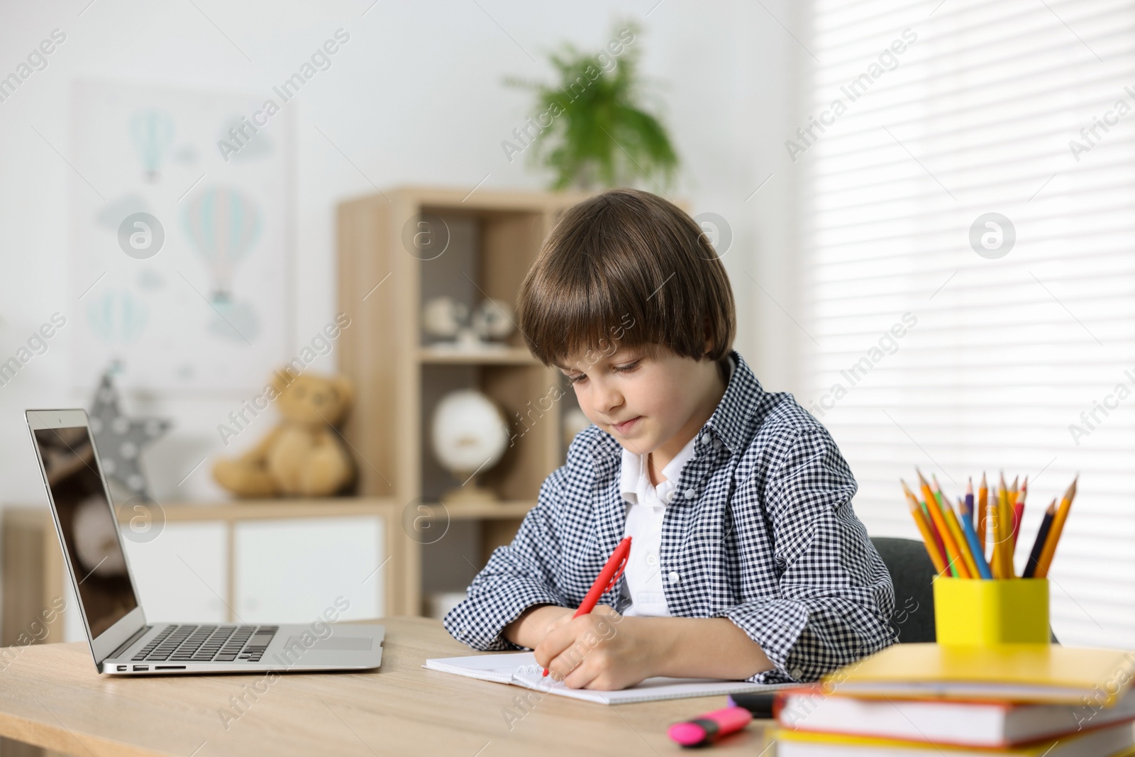 Cute little boy doing homework with laptop at table indoors Photo of Cute little boy doing homework with laptop at table indoors