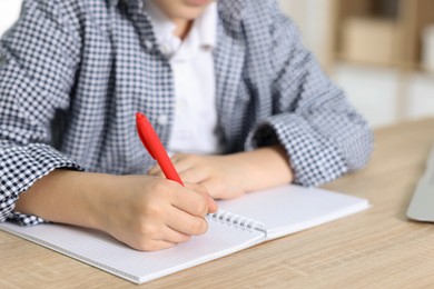 Photo of Little boy doing homework at wooden table indoors, closeup