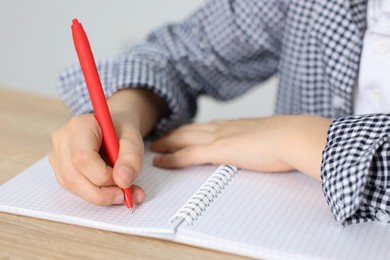 Photo of Little boy doing homework at wooden table indoors, closeup