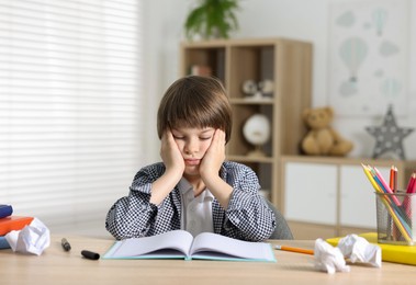 Photo of Tired little boy doing homework at table indoors