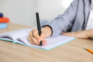Photo of Little boy doing homework at wooden table indoors, closeup