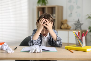 Photo of Tired little boy doing homework at table indoors