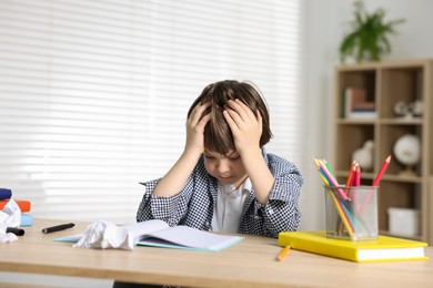 Photo of Tired little boy doing homework at table indoors