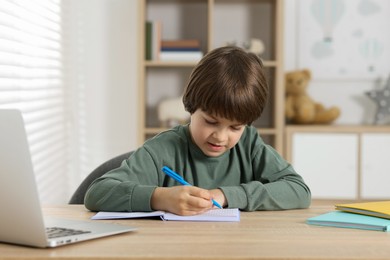 Photo of Cute little boy doing homework at table indoors