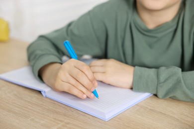 Photo of Little boy doing homework at wooden table indoors, closeup