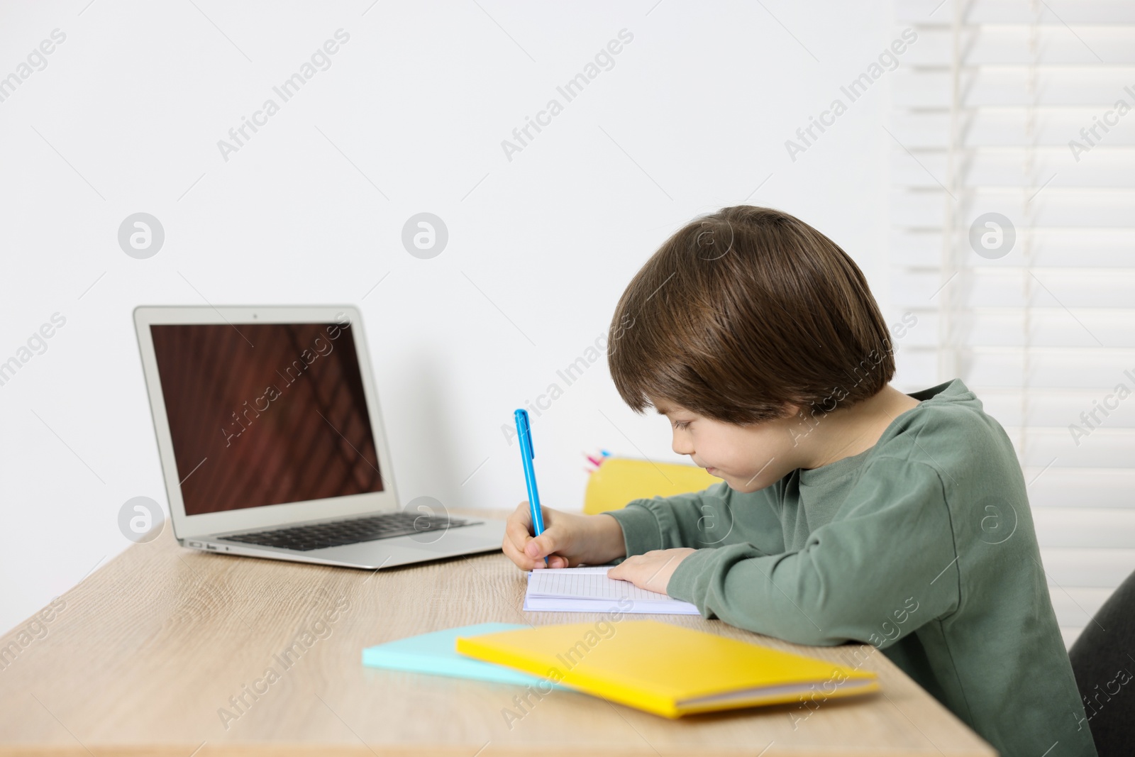 Cute little boy doing homework at table indoors Photo of Cute little boy doing homework at table indoors