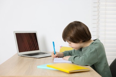 Photo of Cute little boy doing homework at table indoors