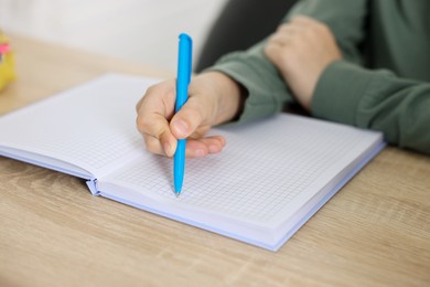 Photo of Little boy doing homework at wooden table indoors, closeup