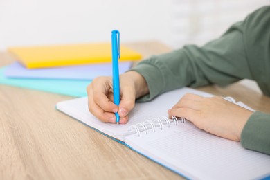 Photo of Little boy doing homework at wooden table indoors, closeup
