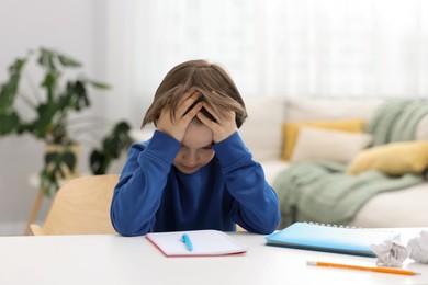 Photo of Tired little boy doing homework at table indoors