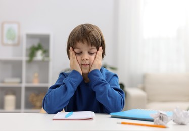 Photo of Tired little boy doing homework at table indoors