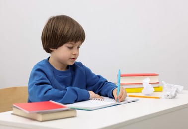 Photo of Cute little boy doing homework at desk indoors