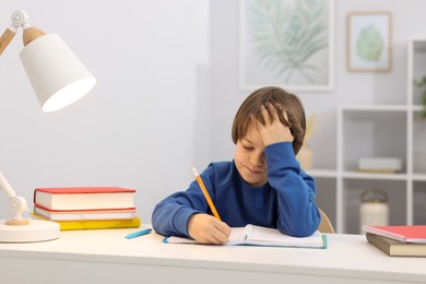 Photo of Cute little boy doing homework at desk indoors