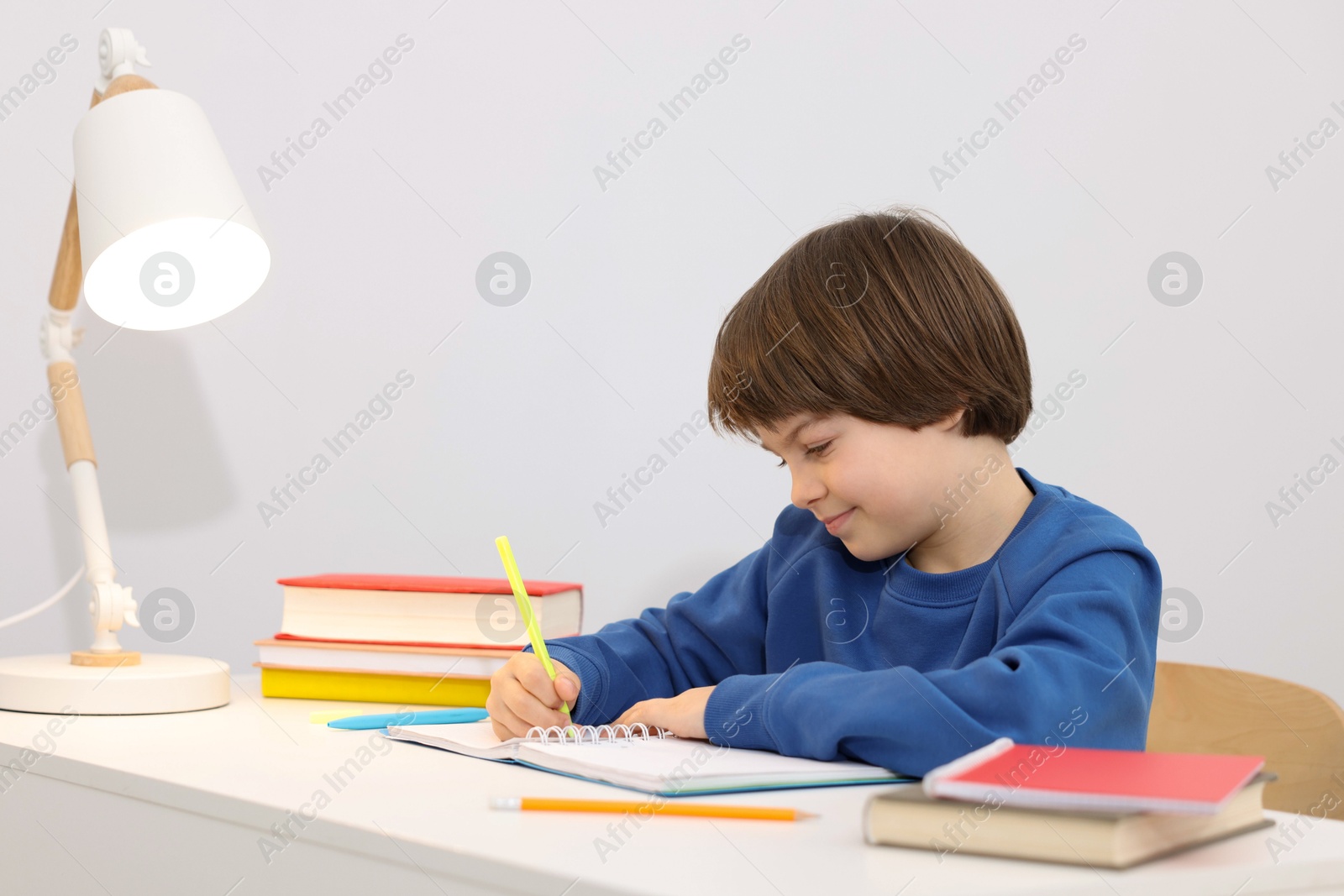 Cute little boy doing homework at desk indoors Photo of Cute little boy doing homework at desk indoors