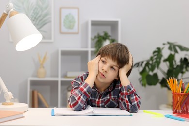 Photo of Tired little boy doing homework at desk indoors