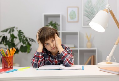 Photo of Tired little boy doing homework at desk indoors