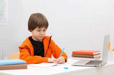 Photo of Cute little boy doing homework at desk indoors