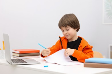 Photo of Cute little boy doing homework at desk indoors