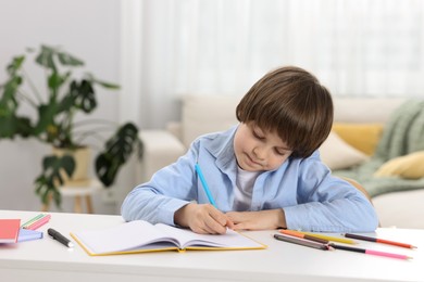 Photo of Cute little boy doing homework at desk indoors