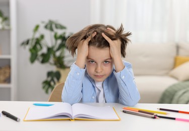 Photo of Tired little boy doing homework at table indoors