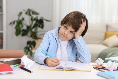 Photo of Tired little boy doing homework at table indoors