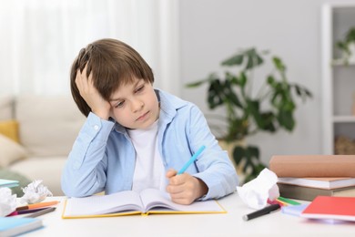Photo of Tired little boy doing homework at table indoors