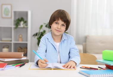 Photo of Cute little boy doing homework at table indoors