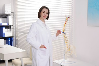 Photo of Doctor pointing at sections of human spine model in clinic