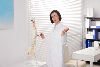Photo of Doctor pointing at sections of human spine model in clinic