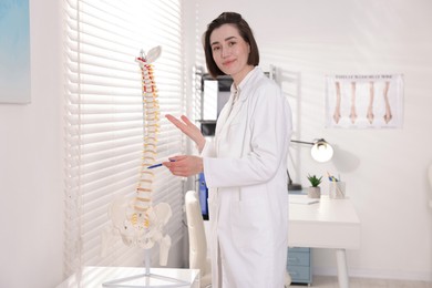 Photo of Doctor pointing at sections of human spine model in clinic