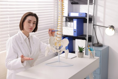 Photo of Doctor pointing at sections of human spine model at desk in clinic