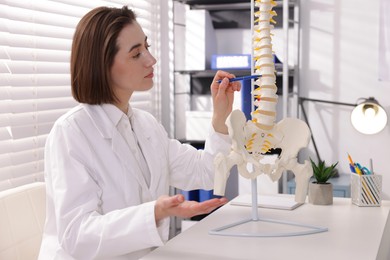 Photo of Doctor pointing at sections of human spine model at desk in clinic