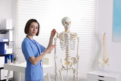 Photo of Doctor pointing at parts of human skeleton model in clinic