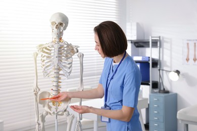 Photo of Doctor pointing at parts of human skeleton model in clinic