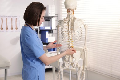Photo of Doctor pointing at parts of human skeleton model in clinic