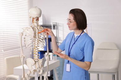 Photo of Doctor pointing at parts of human skeleton model in clinic