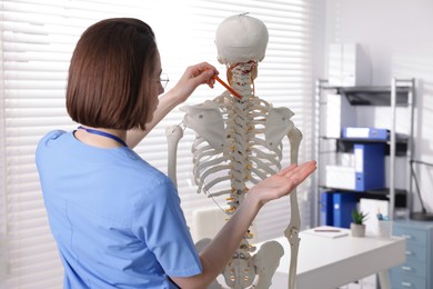 Photo of Doctor pointing at parts of human skeleton model in clinic, back view